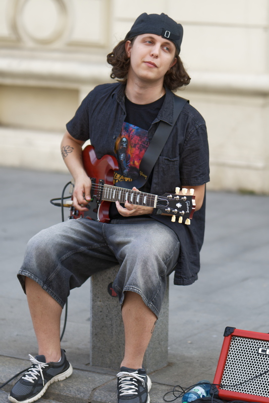 14 - Person playing a red Gibson SG electric guitar while sitting on the street